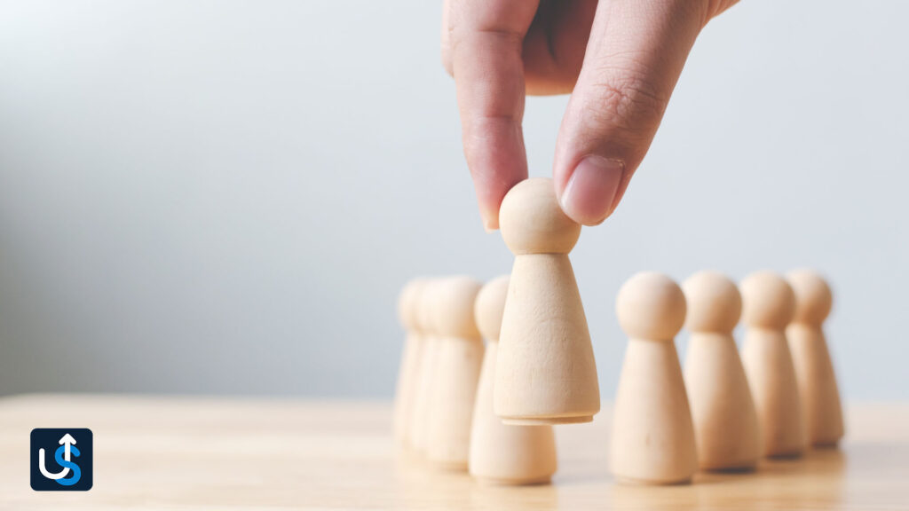 A hand reaching for a wooden figure on a table.