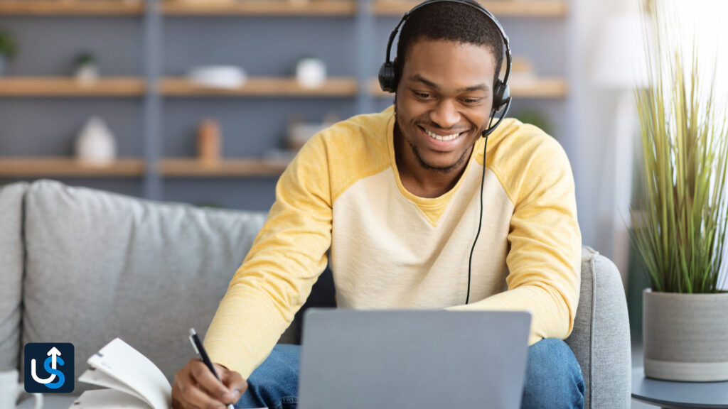 A man wearing headphones and sitting on a couch with a laptop.