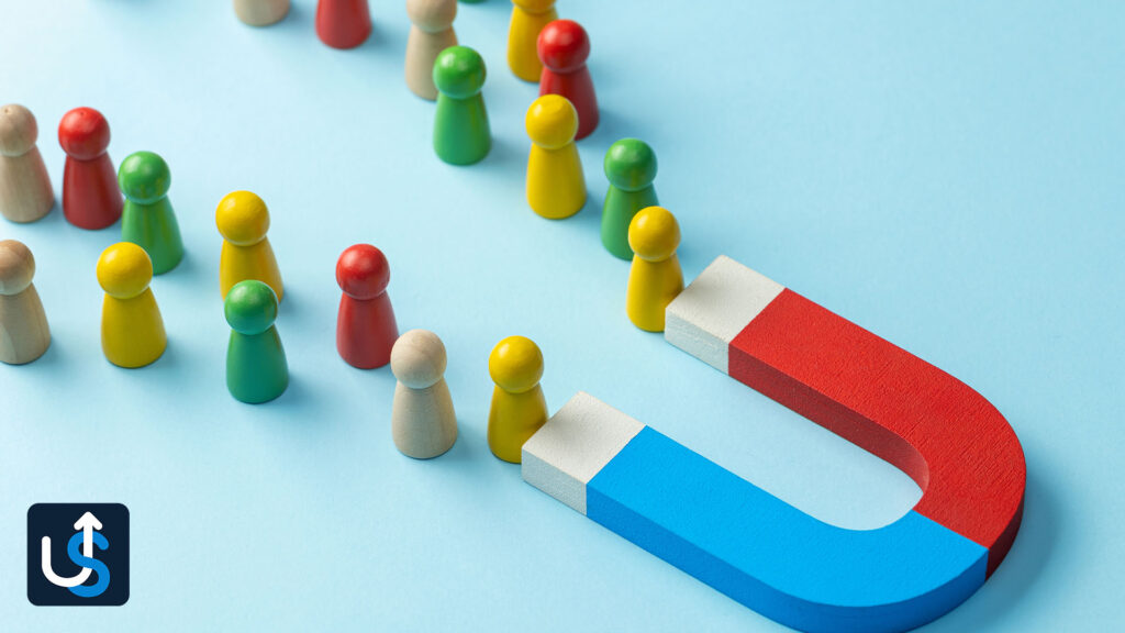 A line of colorful wooden figures being attracted towards a large horseshoe magnet on a blue surface.