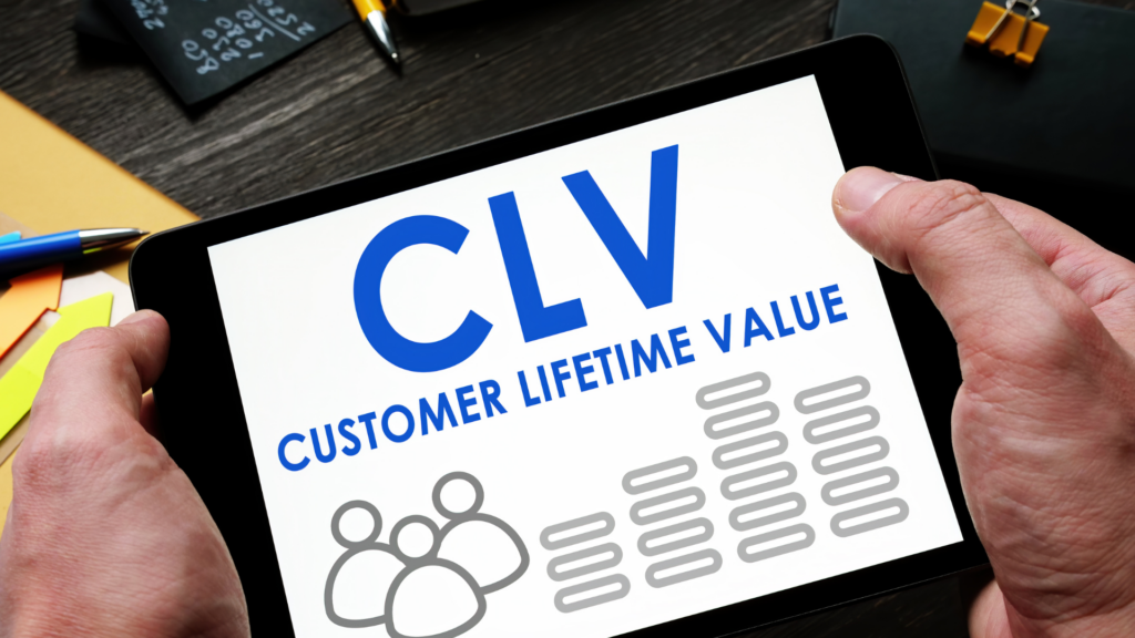 Person holding a tablet displaying "CLV Customer Lifetime Value" with icons of people and bar charts on the screen.