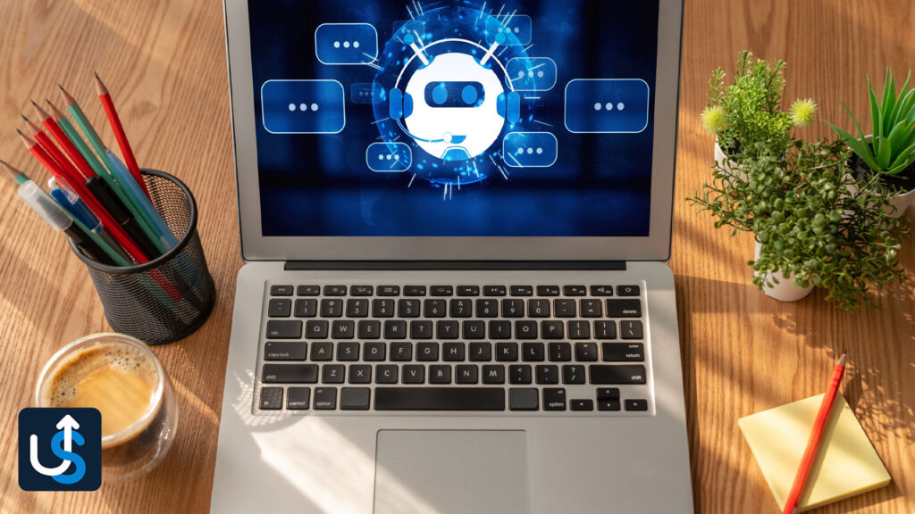 Open laptop on a wooden desk displaying a chatbot icon on the screen, surrounded by coffee, potted plants, pencils, and sticky notes.