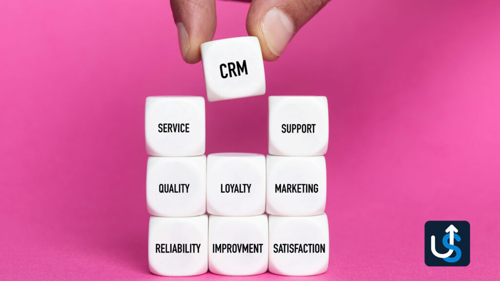 Hand placing a block labeled "CRM" atop a pyramid of blocks labeled with words like "Service," "Support," "Quality," "Loyalty," "Marketing," "Reliability," "Improvement," and "Satisfaction.
