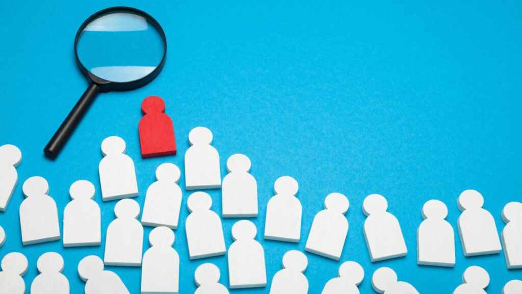 A magnifying glass focuses on a red figure among several white figures on a blue background, emphasizing the standout just like CRM for Agency reveals key insights.