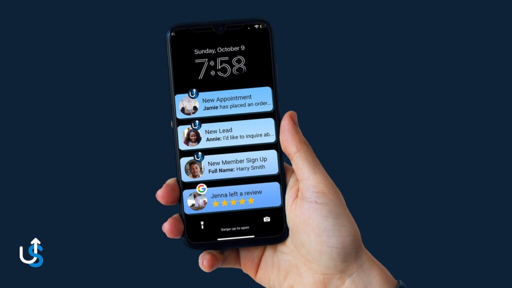 A hand holding a smartphone displaying notifications about a new appointment, a new lead, a new member sign-up, and a review. The screen shows the time as 7:58 and the date as Sunday, October 9.