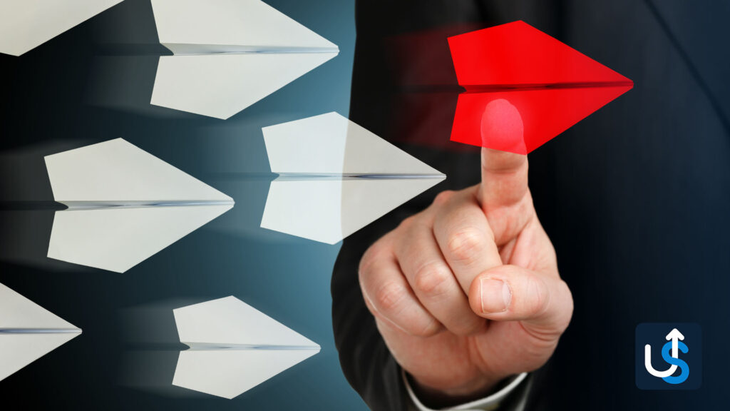 A person in a suit presses a red paper airplane icon among white paper airplanes, symbolizing leadership or standing out. An upward arrow logo is in the bottom-right corner.