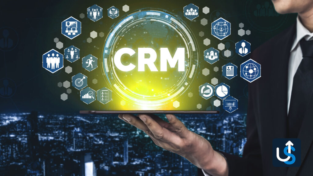 Person holding a digital tablet displaying a CRM (Customer Relationship Management) interface with various icons related to business functions, against a cityscape background.