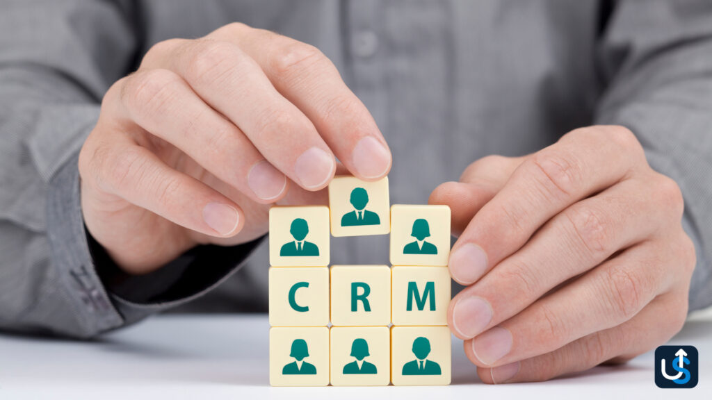 Hands arranging letter tiles with "CRM" and icons of people on them in a grid on a table.