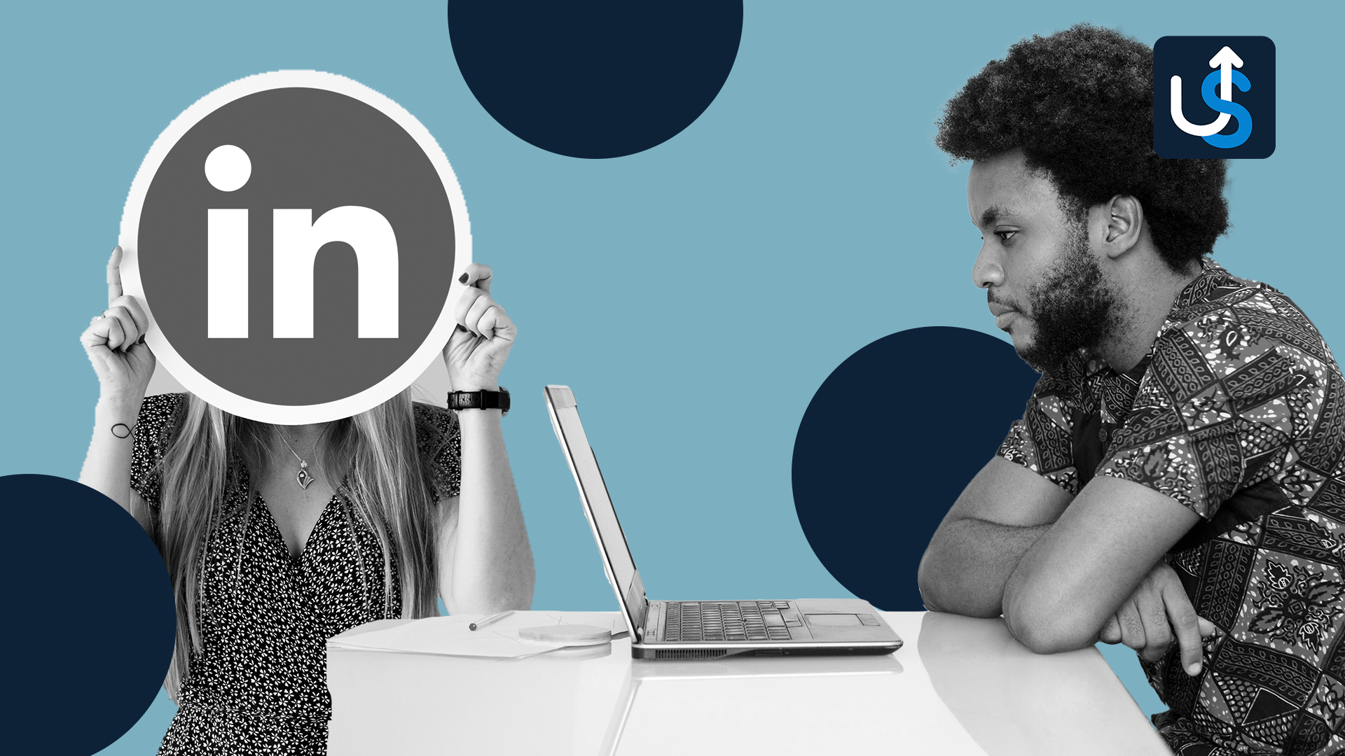 A woman holds a LinkedIn logo over her face while sitting at a desk with a laptop. A man sits across from her, looking at the laptop.