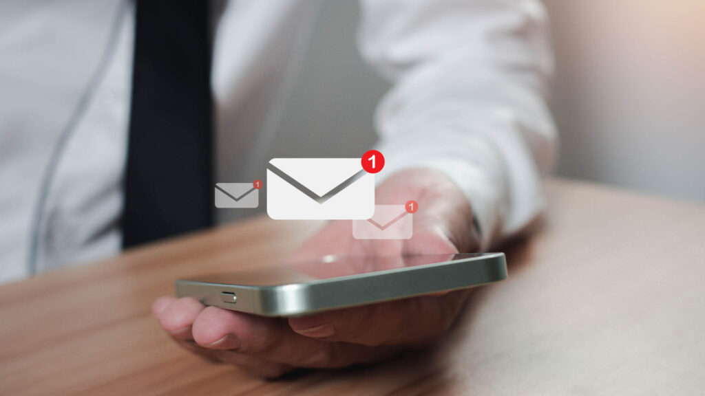 A hand holds a smartphone displaying an email icon with a notification badge indicating new messages.