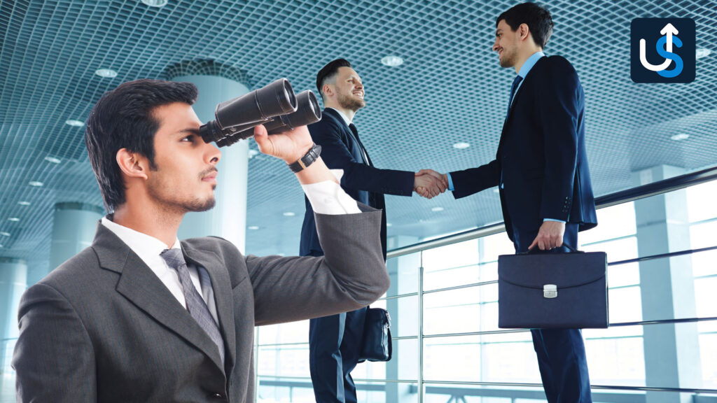 A businessman looks through binoculars in the foreground, while two other businessmen in suits shake hands in a modern office setting.